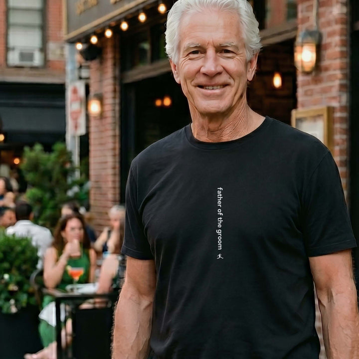 Man wearing a Bored Rebel black crewneck graphic t-shirt at an upscale outdoor restaurant. The minimalist vertical saying on the front reads &