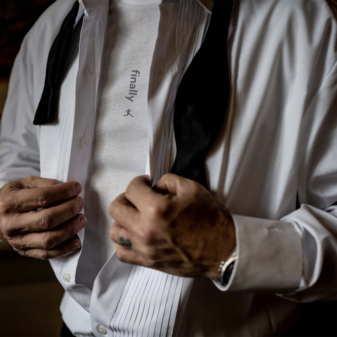 A groom buttoning his tux shirt, revealing a Bored Rebel men&