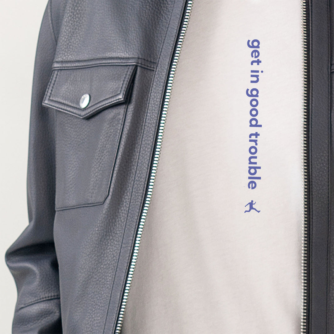Close-up of a navy Hugo Boss leather jacket worn over a white Bored Rebel T-shirt. The T-shirt features a vertical saying that reads 'get in good trouble'.