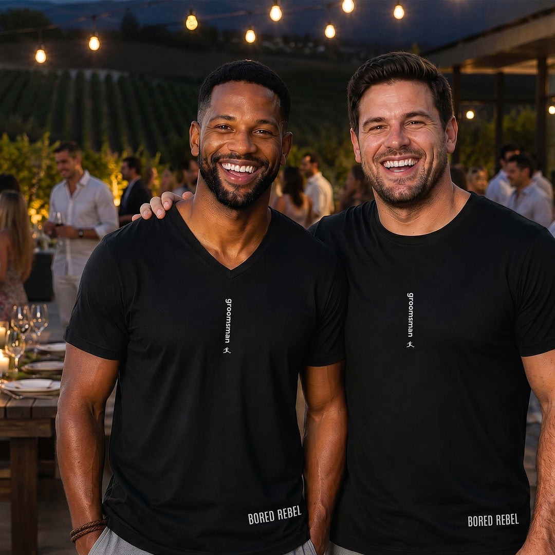 Two men at a vineyard party in black Bored Rebel graphic tees — one crewneck, one V-neck — featuring a minimalist vertical saying on their chests that reads &