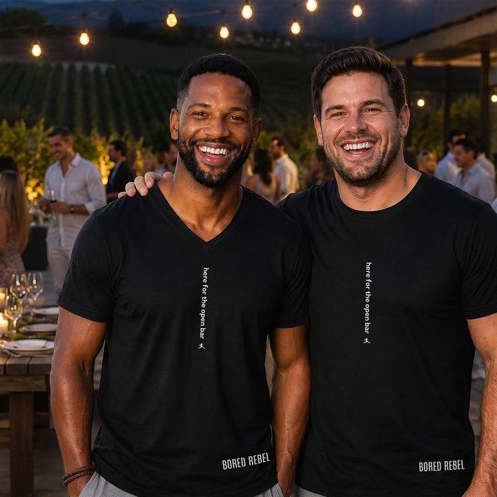 Two men at a vineyard party in black Bored Rebel graphic tees — one crewneck, one V-neck — featuring a minimalist vertical saying on their chests that reads &
