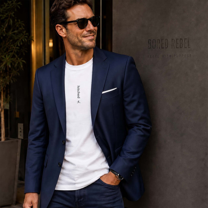 Man wearing a white Bored Rebel graphic tee and a sports coat leaning on an upscale building. The minimalist vertical saying on his chest reads "hitched".
