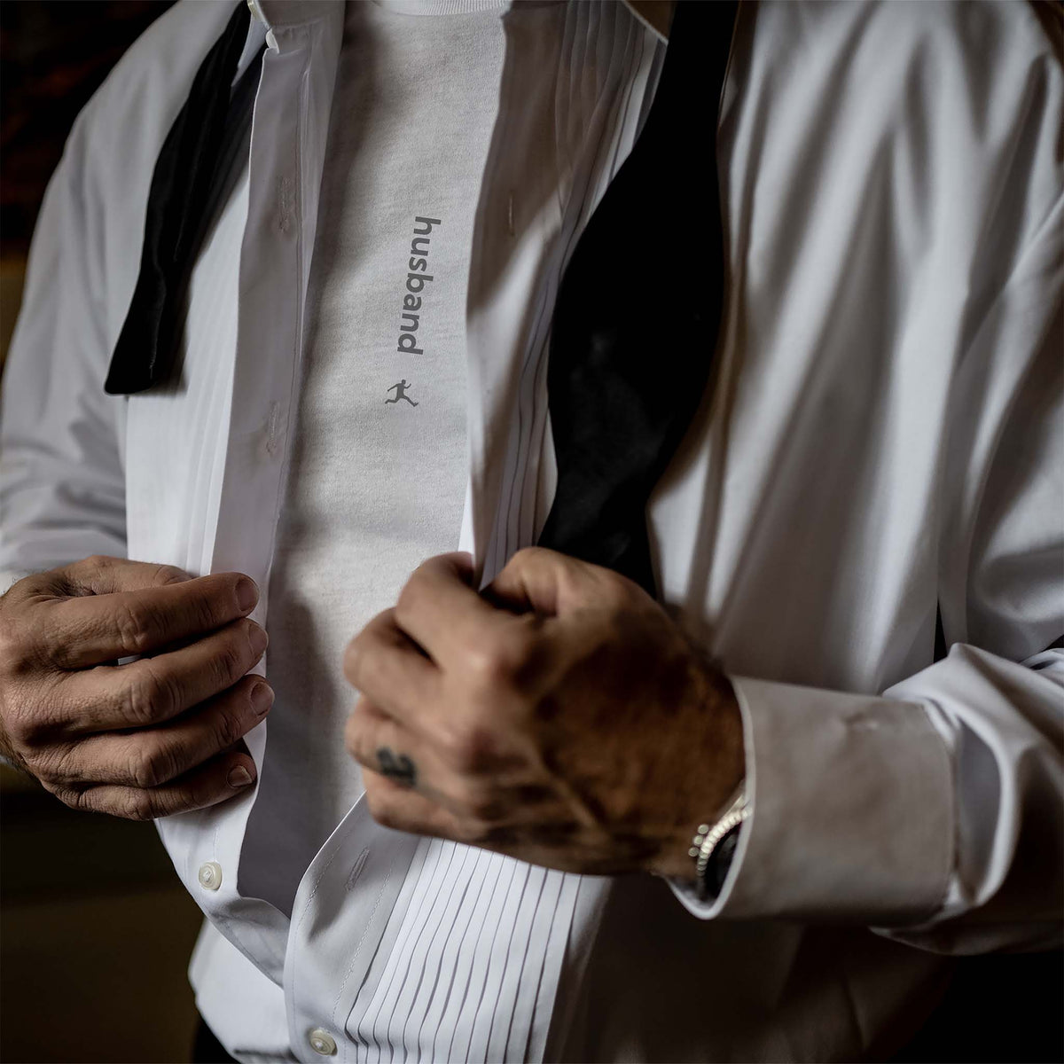 A groom buttoning his tuxedo shirt and revealing a Bored Rebel Husband Graphic Undershirt underneath.
