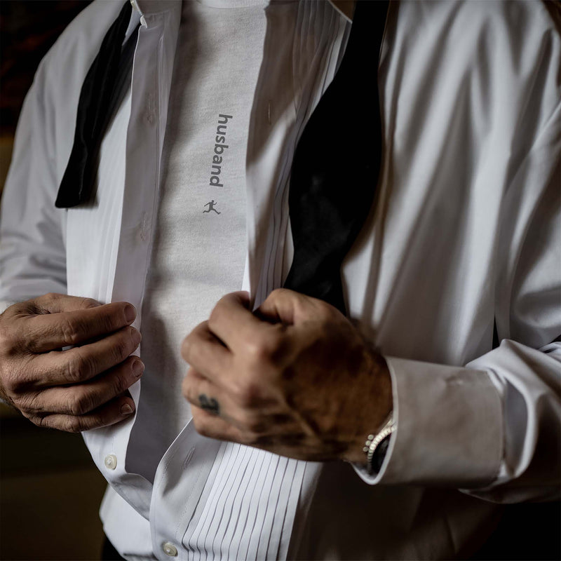 A groom buttoning his tuxedo shirt and revealing a Bored Rebel Husband graphic undershirt underneath.