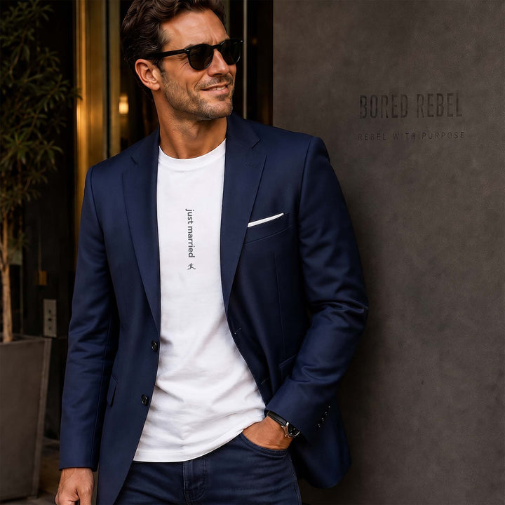 Man wearing a white Bored Rebel graphic tee and a sports coat leaning on an upscale building. The minimalist vertical saying on his chest reads Just Married
