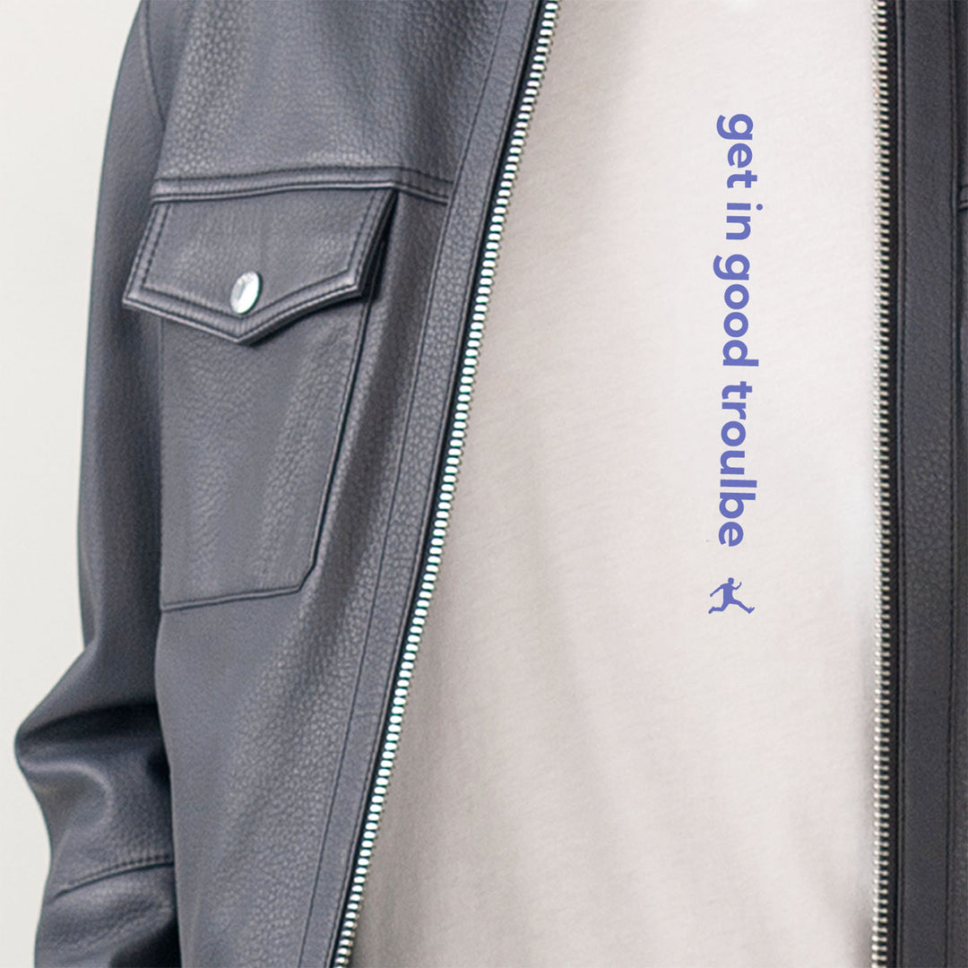 Close-up of a navy Hugo Boss leather jacket worn over a white Bored Rebel T-shirt. The T-shirt features a vertical saying that reads 'get in good trouble'.