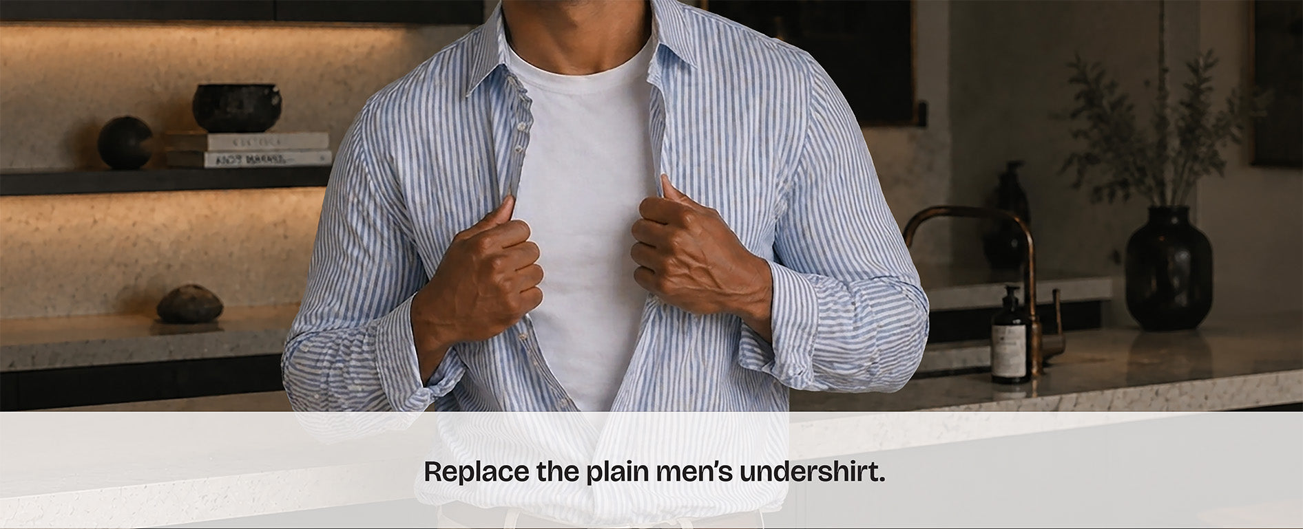 Man opens his dress shirt superman style to reveal an undershirt. Text overlay reads 'replace the plain men's undershirt'. He's in an upscale modern kitchen.