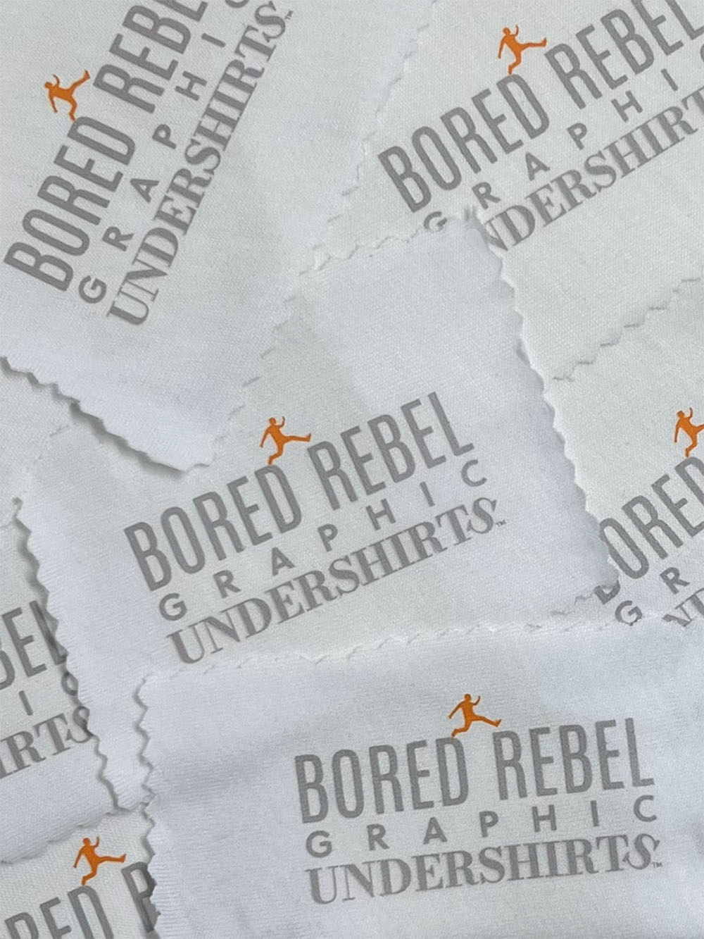 Multiple pieces of white fabric with 'Bored Rebel Graphic Undershirts' grey text and an orange logo.