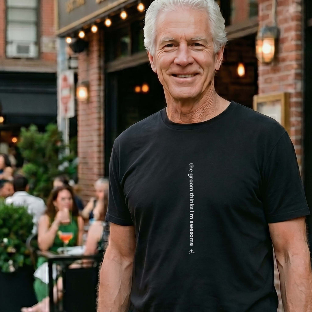 Man wearing a Bored Rebel black crewneck graphic t-shirt at an upscale outdoor restaurant. The minimalist vertical saying on the front reads &