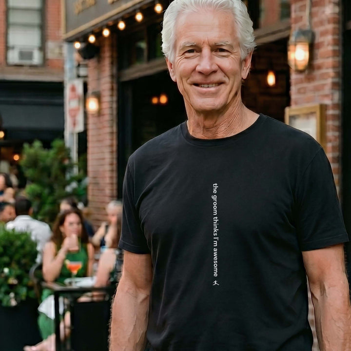 Man wearing a Bored Rebel black crewneck graphic t-shirt at an upscale outdoor restaurant. The minimalist vertical saying on the front reads &