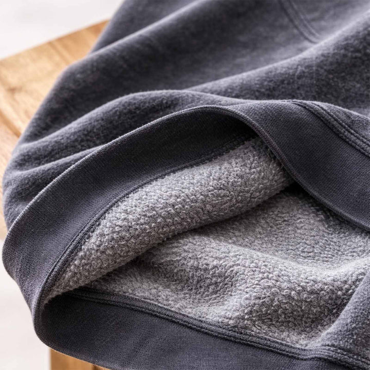 Dark grey vintage wash sweatshirt laying on a maple stool, with the inside fluffy fleece showing.