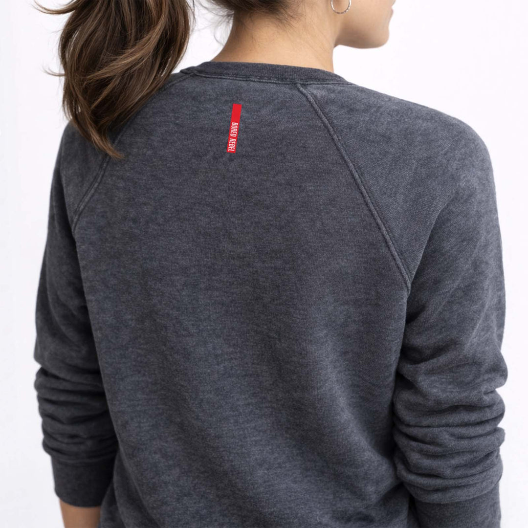 Back of a vintage wash dark grey sweatshirt. A small vertical red logo with white text reads 'Bored Rebel'.